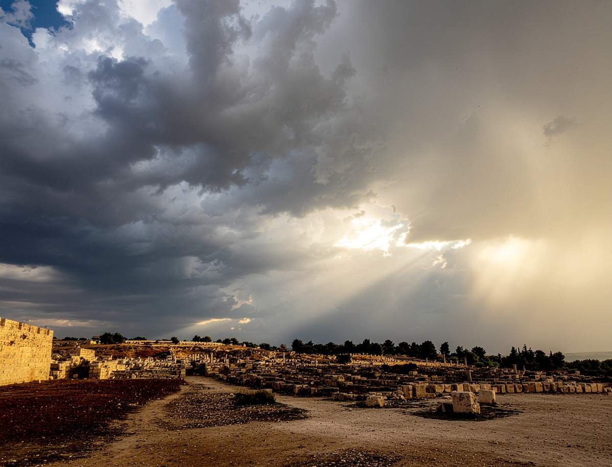 Dramatic golden light breaking through dark clouds over ancient landscape