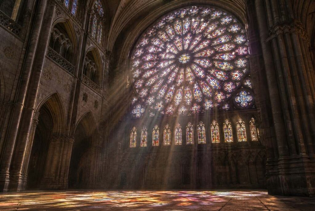 Sunlight streaming through a Gothic rose window, illuminating cathedral interior with coloured light patterns
