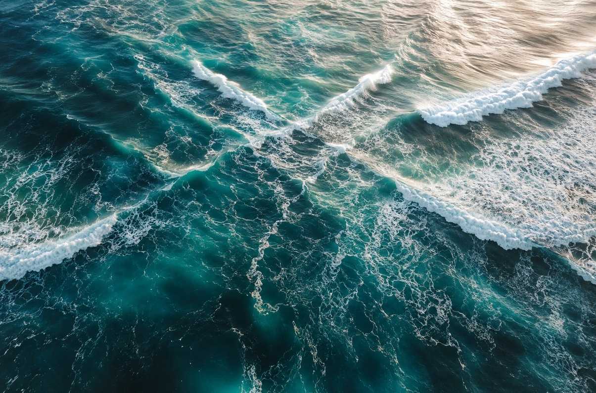 Aerial view of ocean waves crashing from opposite directions creating interference patterns