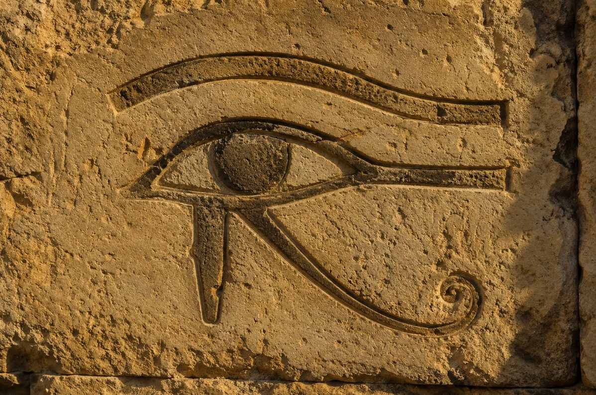 An ancient Egyptian Eye of Horus symbol carved in stone, illuminated by warm golden light, symbolising restored wholeness of perception
