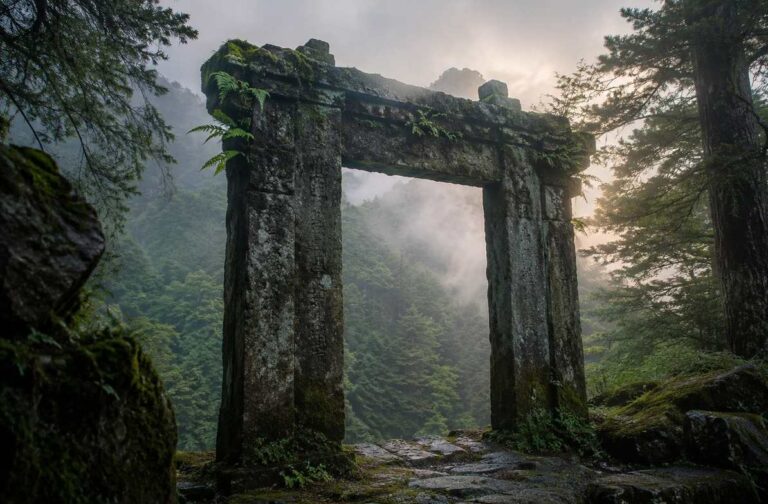 Ancient moss-covered stone gate with no doors standing in misty mountain forest at dawn