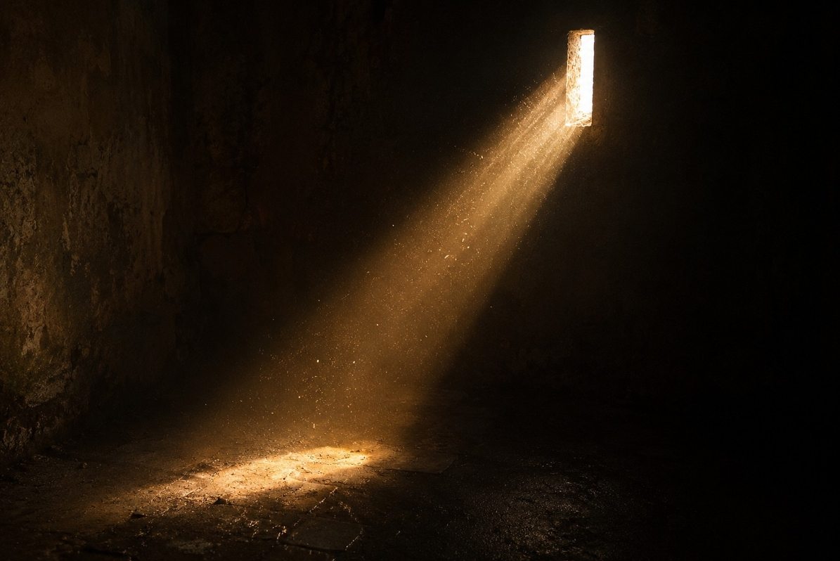 A narrow beam of light passing through a small aperture into a darkened room, revealing dust motes and hidden textures, symbolising the visible slit and the hidden field beyond